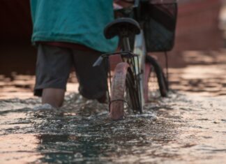 Un uomo spinge la bici in mezzo all'acqua di un'esondazione