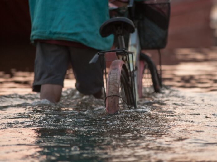 Un uomo spinge la bici in mezzo all'acqua di un'esondazione